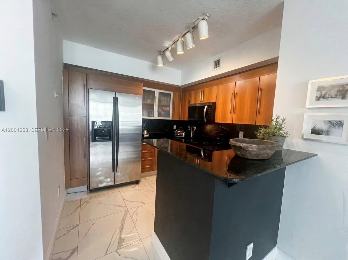 A kitchen features wood cabinets, stainless steel appliances, a black countertop, and white tile flooring — 335 S Biscayne Blvd # 3300, Miami FL 33131, MIAMI, FL