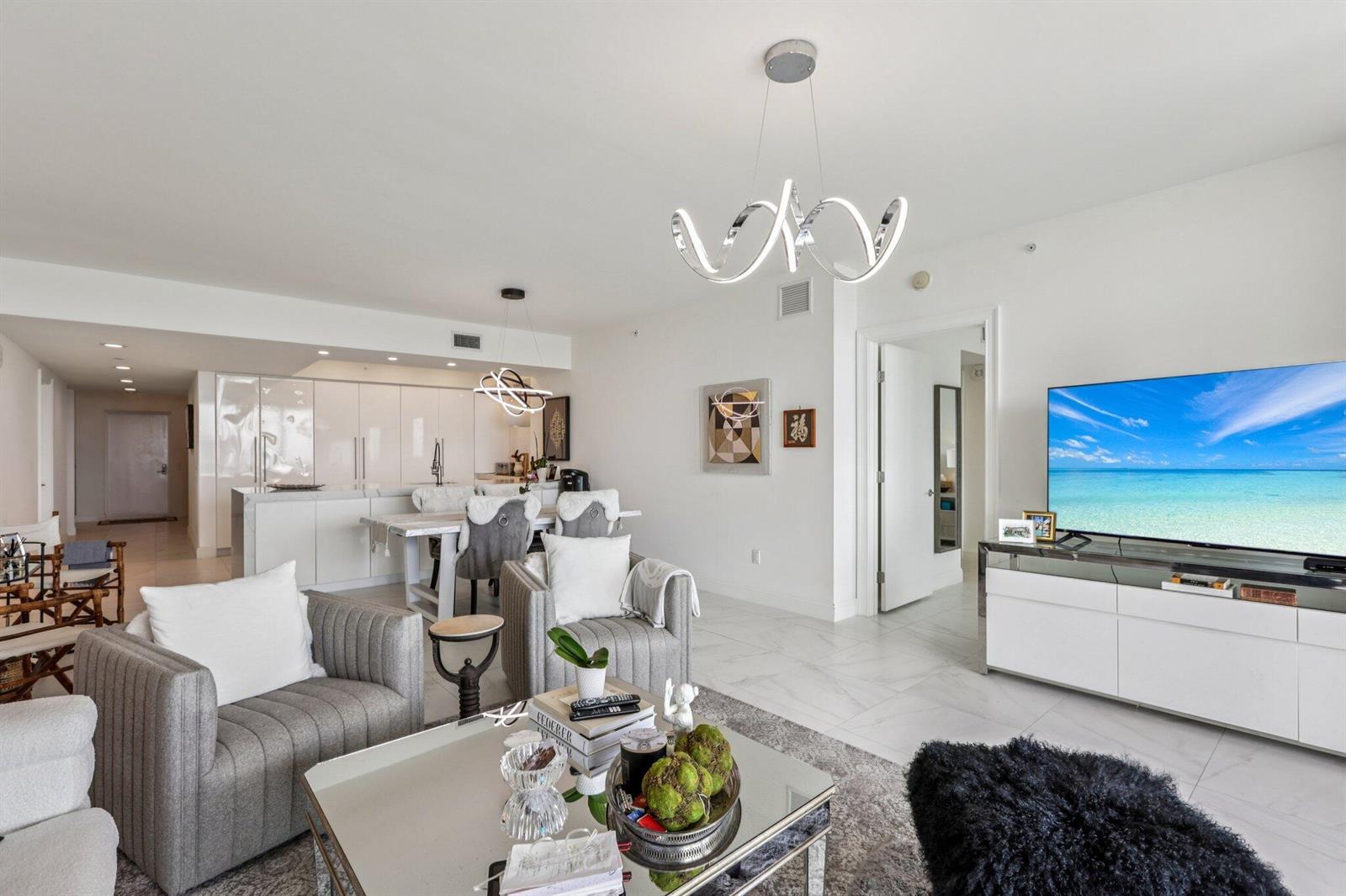 A modern living room and kitchen area with white cabinetry, tile floors, and contemporary lighting — 2640 Lake Shore Drive # 2008, Riviera Beach FL 33404, RIVIERA BEACH, FL