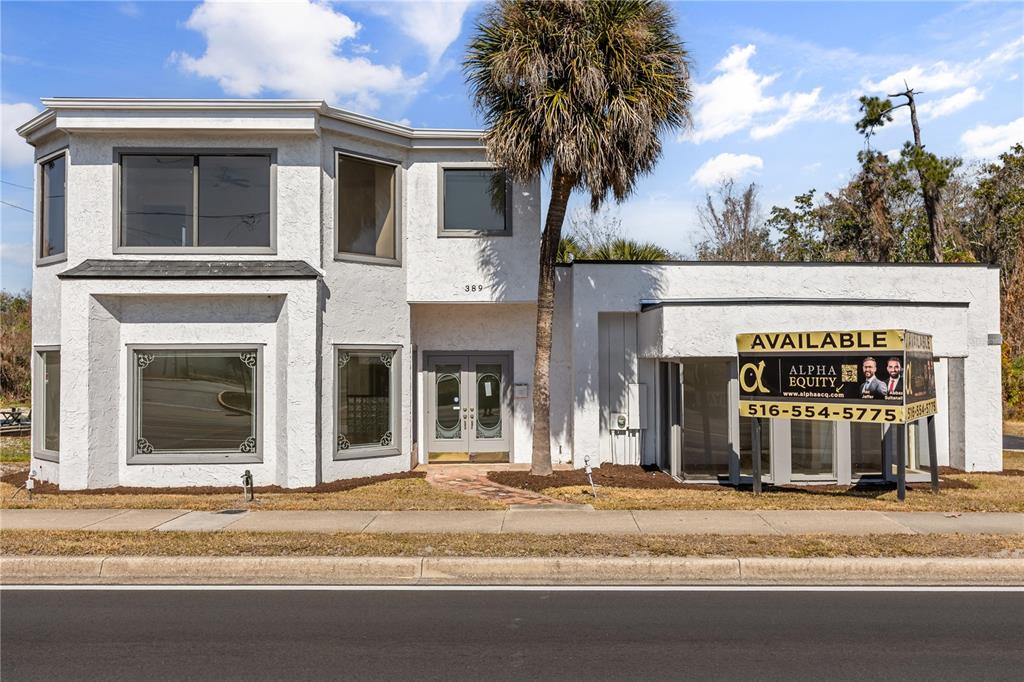 A two-story white stucco commercial building features a palm tree and a real estate sign — 389 E STATE ROAD 434, LONGWOOD, FL