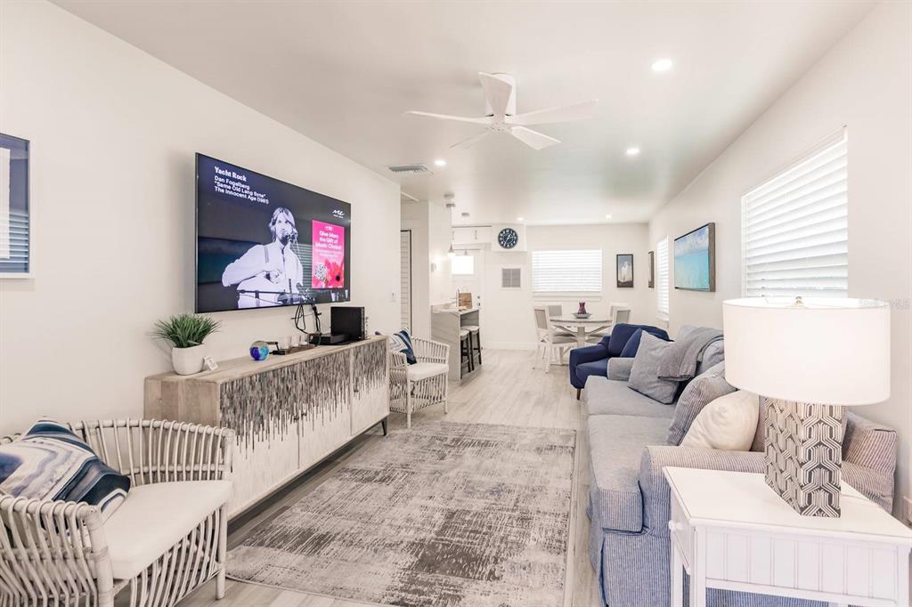 A living room with a television, a blue sofa, white chairs, and light wood flooring — 6020 MIDNIGHT PASS ROAD UNIT 12, SARASOTA, FL