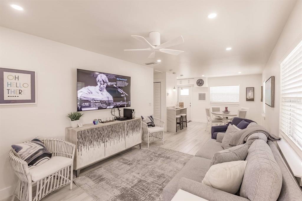 A living room with a gray sofa, white wicker chairs, a television, and light flooring — 6020 MIDNIGHT PASS ROAD UNIT 12, SARASOTA, FL