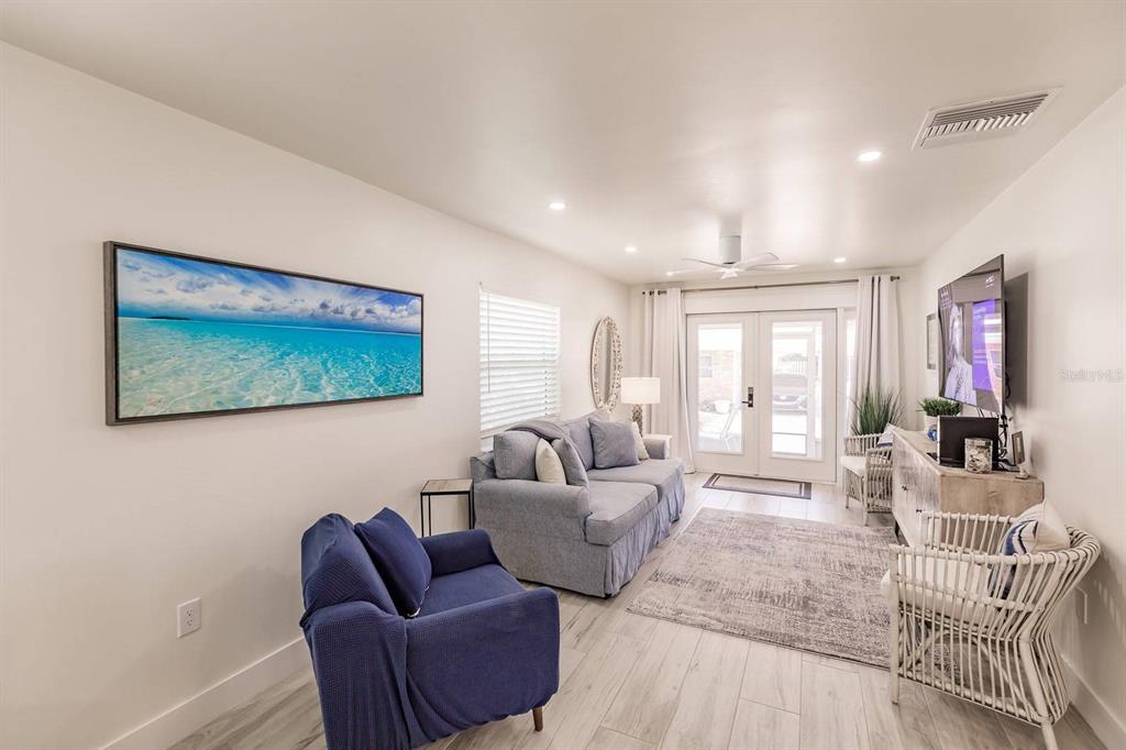 A living room features a blue sofa, a matching armchair, and a wall-mounted television — 6020 MIDNIGHT PASS ROAD UNIT 12, SARASOTA, FL