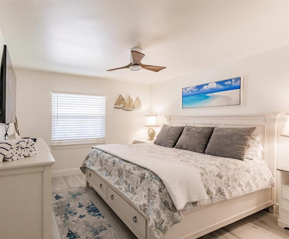 A bedroom features a king bed with a coastal-themed quilt, a ceiling fan, and white furniture — 6020 MIDNIGHT PASS ROAD UNIT 12, SARASOTA, FL