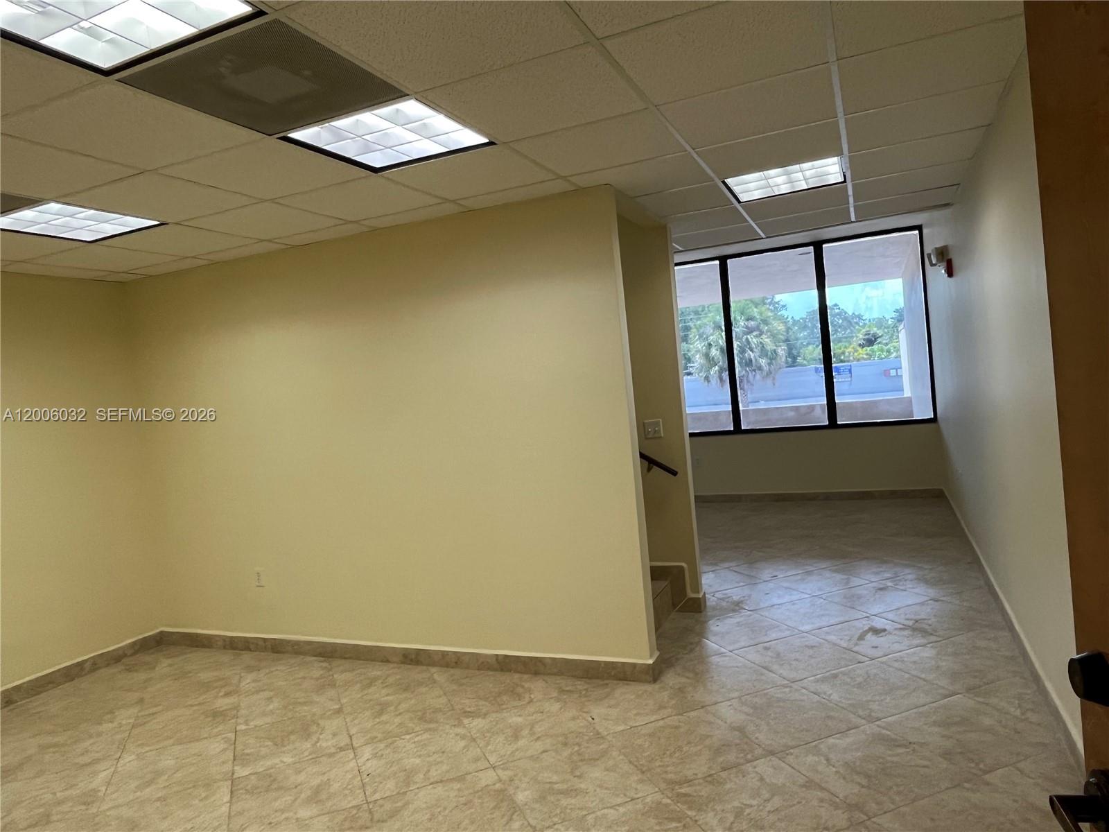 An empty office space features beige walls, tiled floors, drop ceilings, and large windows — 5455 SW 8 ST # 215, Miami FL 33134, MIAMI, FL