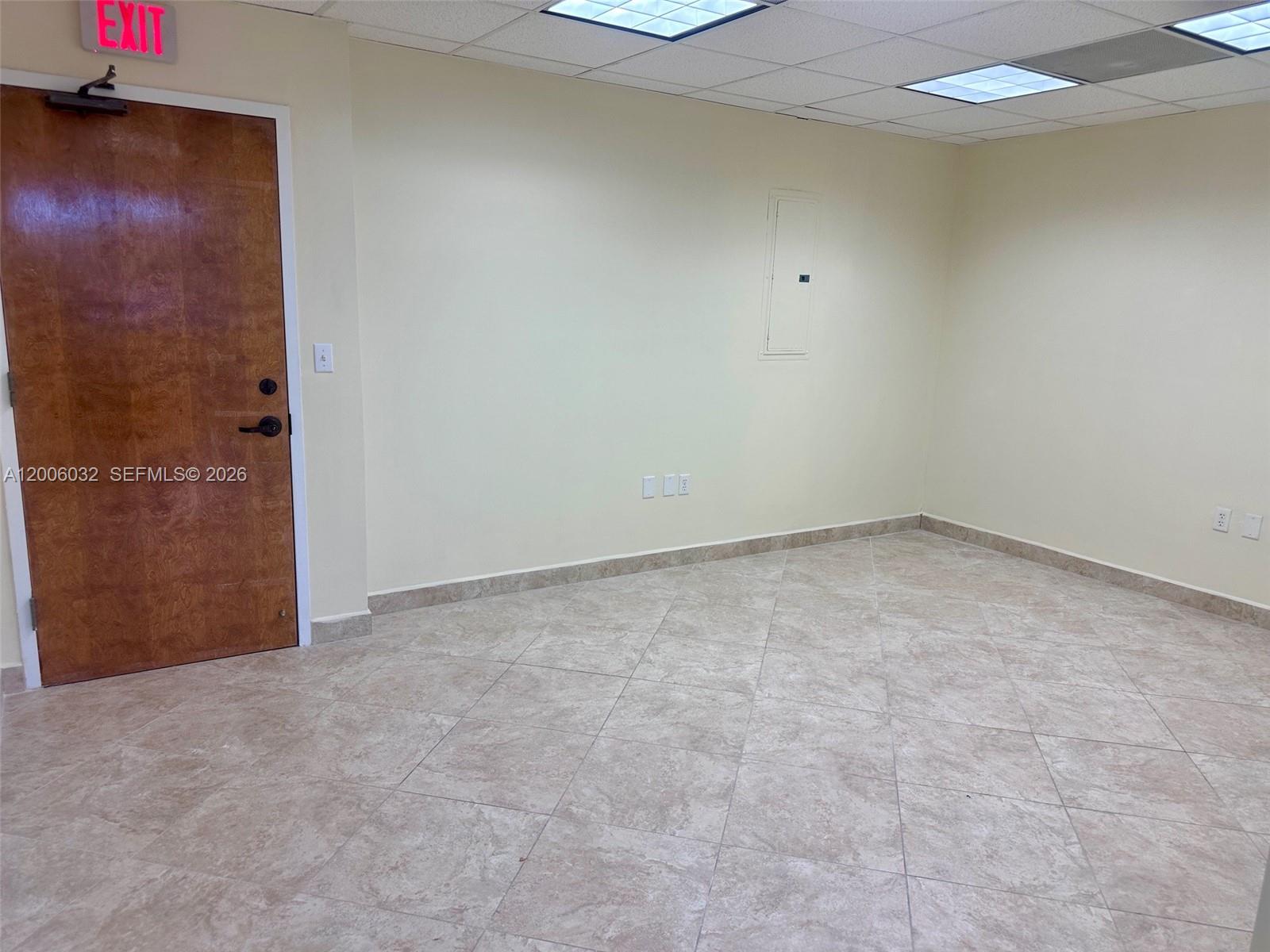 An empty office room features light-colored walls, tiled flooring, a wooden door, and ceiling lights — 5455 SW 8 ST # 215, Miami FL 33134, MIAMI, FL