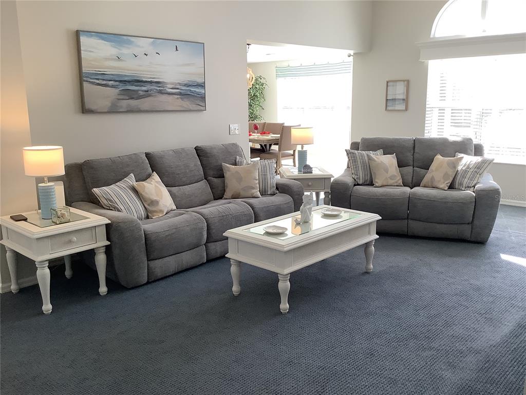 A living room features two gray sofas, a white coffee table, and blue carpeting — 890 HAYNESVILLE WAY, THE VILLAGES, FL