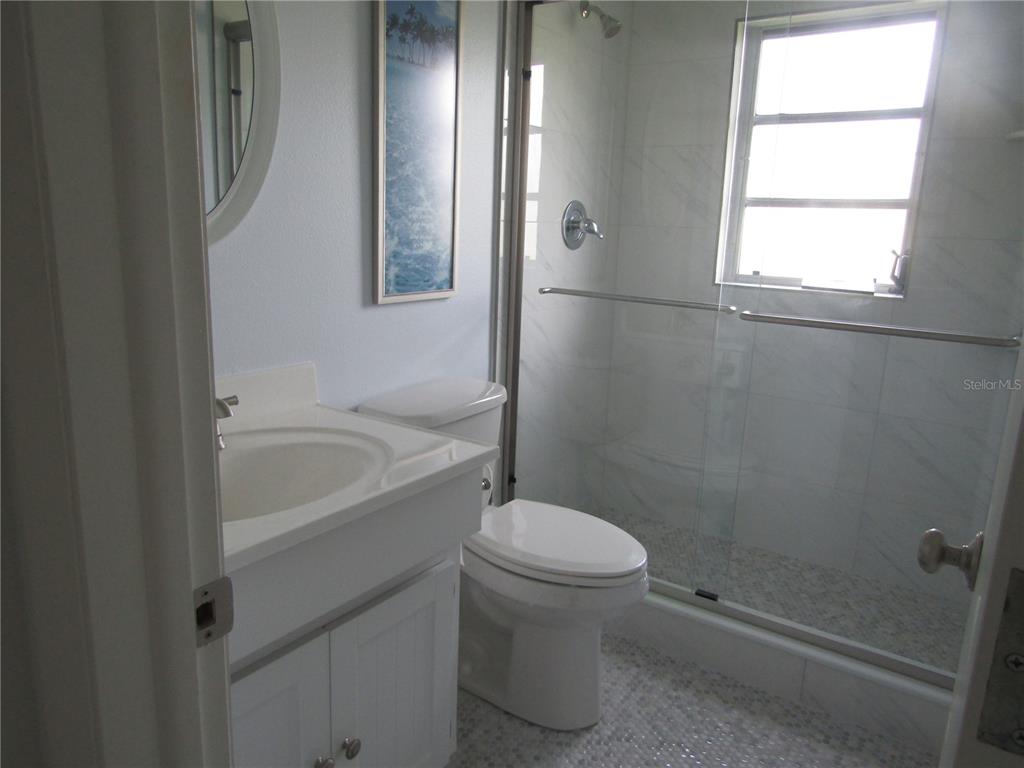 A bathroom features a white vanity, a toilet, and a glass-enclosed shower with tiled walls — 7008 W COUNTRY CLUB DRIVE N UNIT 136, SARASOTA, FL