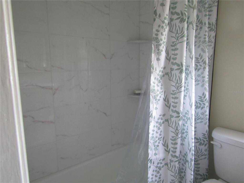 A bathroom features a white marble-tiled shower with built-in shelves and a patterned shower curtain — 7008 W COUNTRY CLUB DRIVE N UNIT 136, SARASOTA, FL