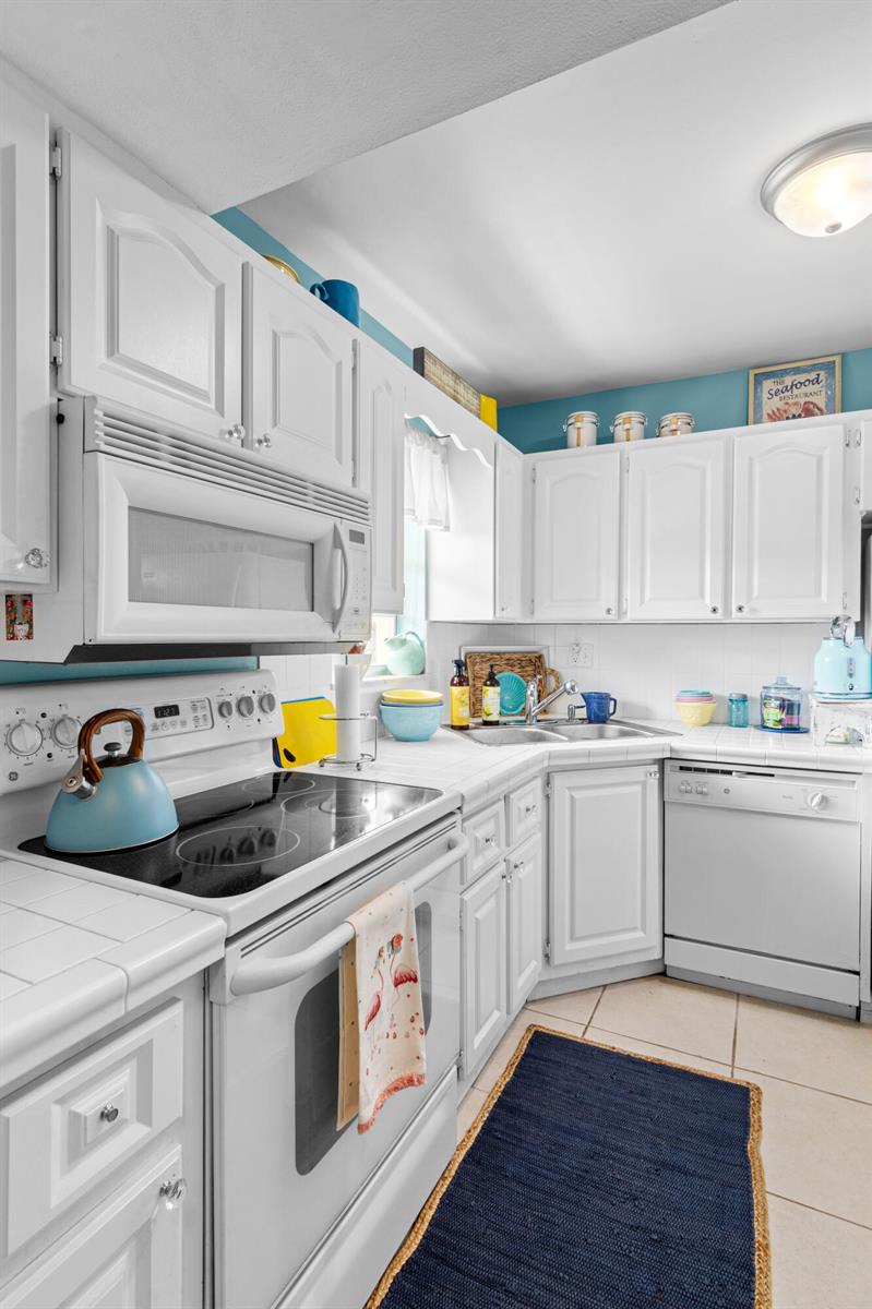 A kitchen features white cabinets, white appliances, tiled countertops, and blue wall accents — 1967 SW Palm City Road # h, Stuart FL 34994, STUART, FL