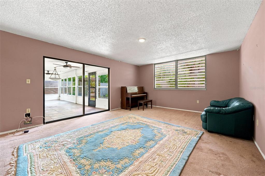 A living room with mauve walls, a patterned area rug, a piano, and sliding glass doors — 240 SHERWOOD DRIVE, BRADENTON, FL