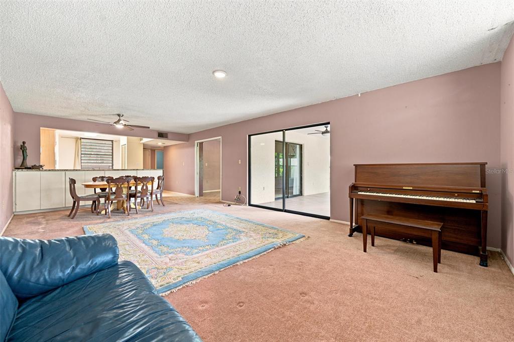 A living room features mauve walls, a piano, a blue area rug, and a dining area — 240 SHERWOOD DRIVE, BRADENTON, FL