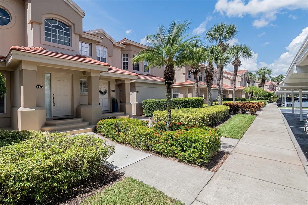 A row of tan townhouses with red tile roofs and palm trees along a sidewalk — 447 ENCLAVE PLACE UNIT 447, LAKELAND, FL
