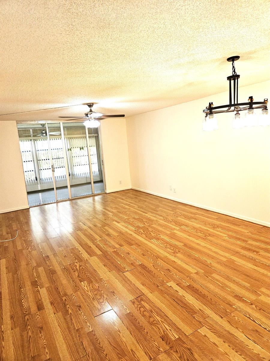 An empty living room with wood-look flooring, a ceiling fan, and a sliding glass door — 357 N Rock Island Road # 407, Margate FL 33063, MARGATE, FL