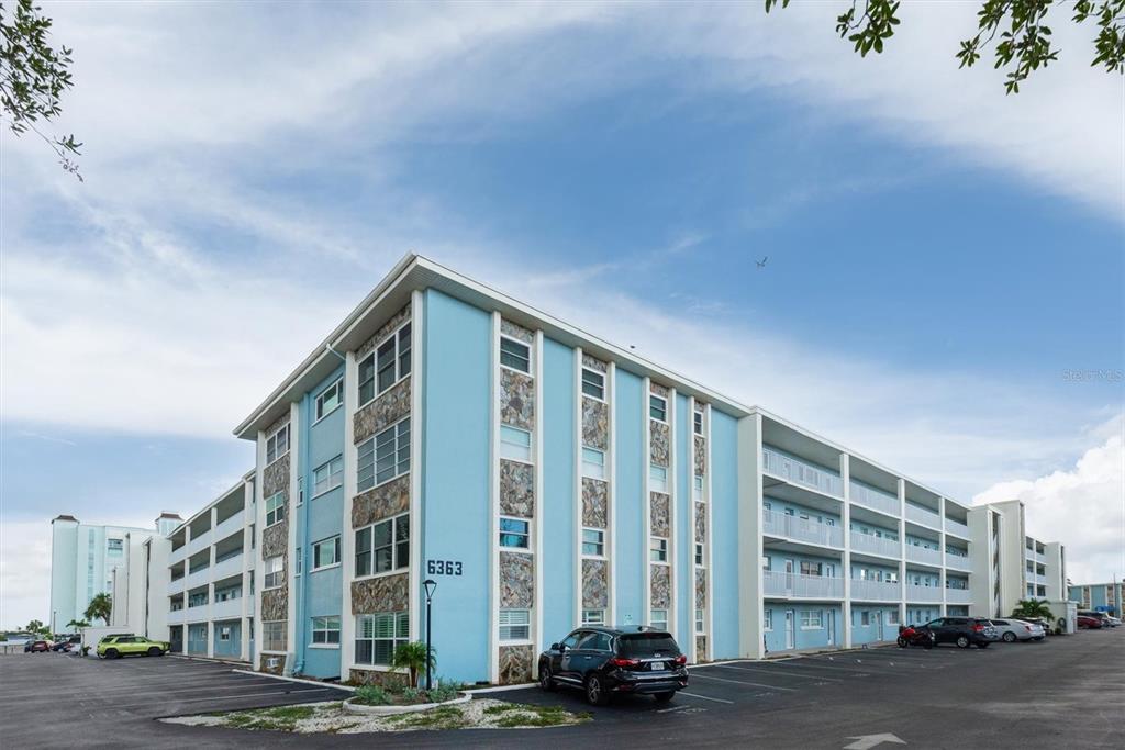 A multi-story blue apartment building with stone accents and a parking lot in front — 6363 GULF WINDS DRIVE UNIT 233, ST PETERSBURG, FL