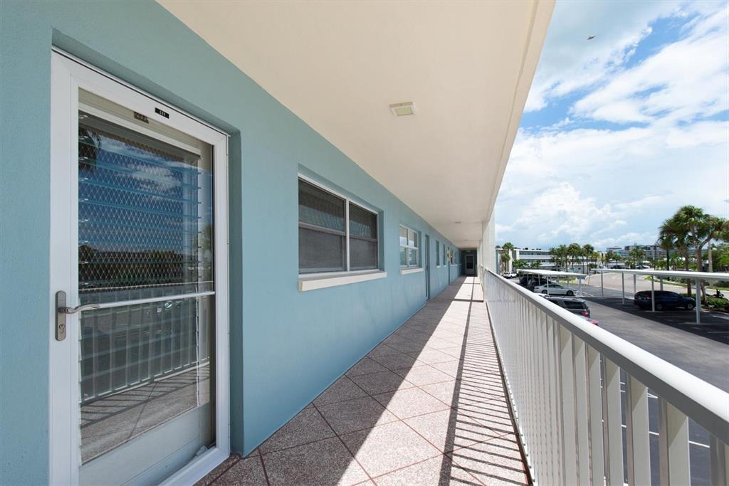 An outdoor walkway with a white railing overlooks a parking lot beside a blue building — 6363 GULF WINDS DRIVE UNIT 233, ST PETERSBURG, FL