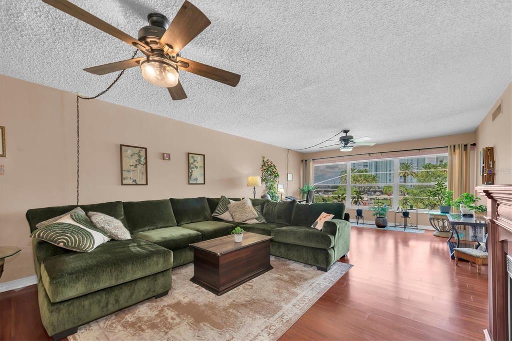A living room features a large green sectional sofa, wood flooring, and a ceiling fan — 6363 GULF WINDS DRIVE UNIT 233, ST PETERSBURG, FL