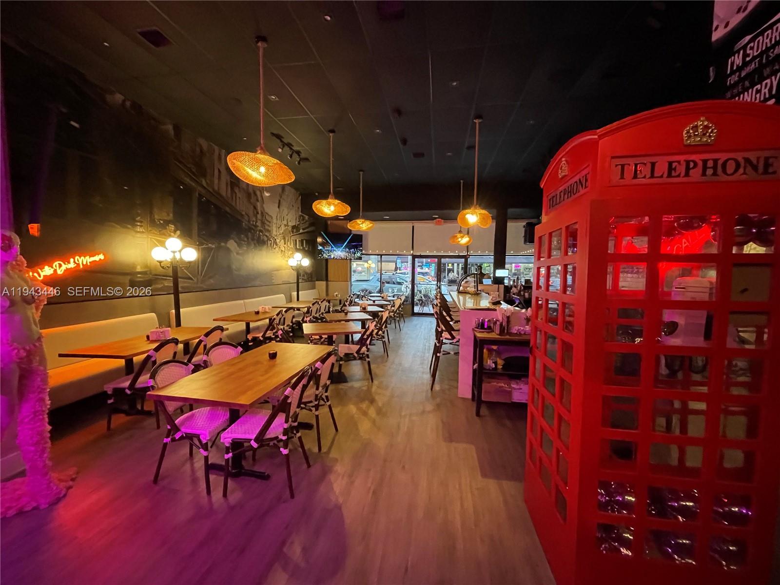 A restaurant interior features wooden tables, woven chairs, hanging pendant lights, and a red telephone booth — 310 71st St, Miami Beach FL 33141, MIAMI BEACH, FL