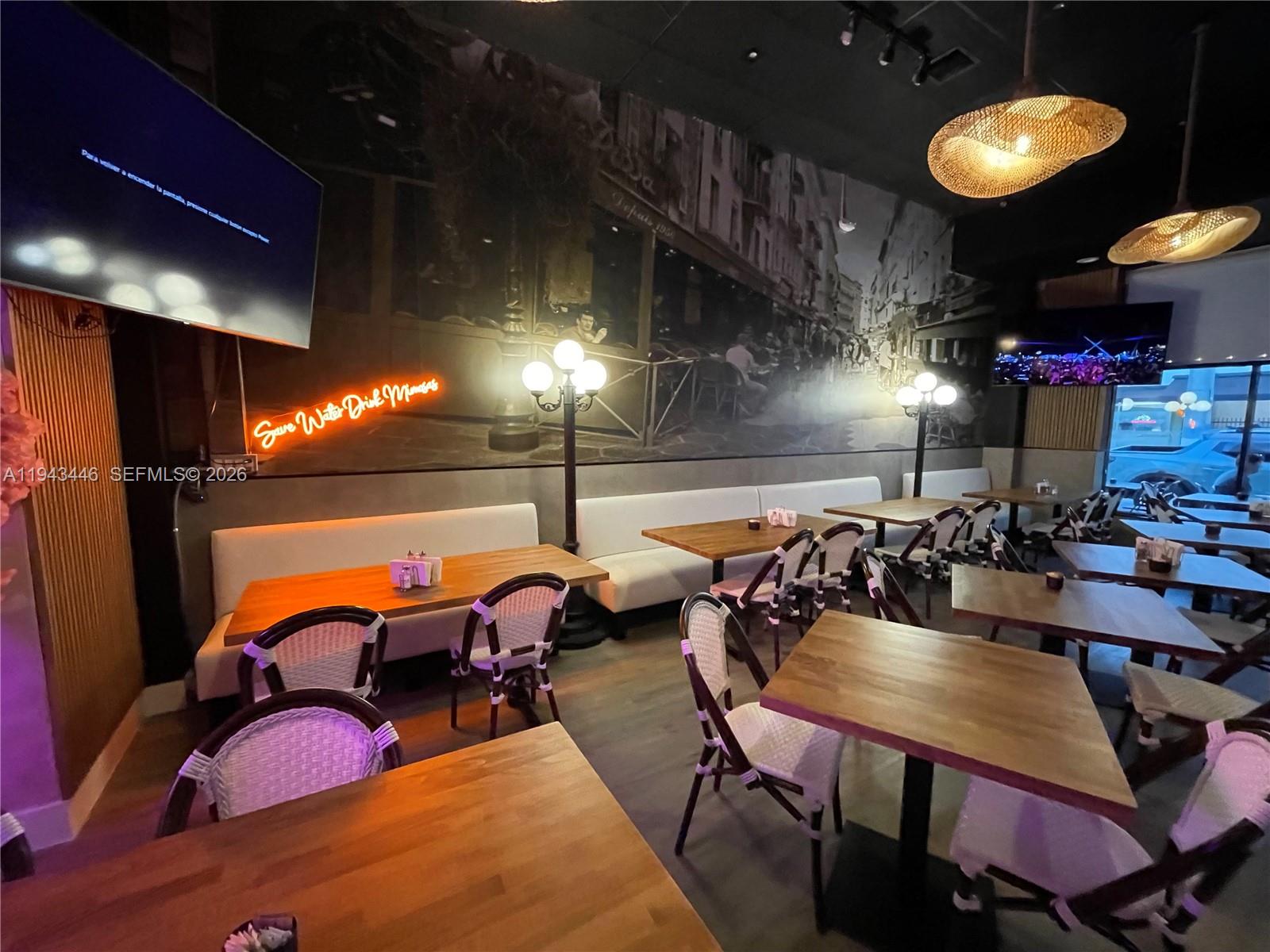 A restaurant interior features wooden tables, white chairs, a large wall mural, and neon signage — 310 71st St, Miami Beach FL 33141, MIAMI BEACH, FL
