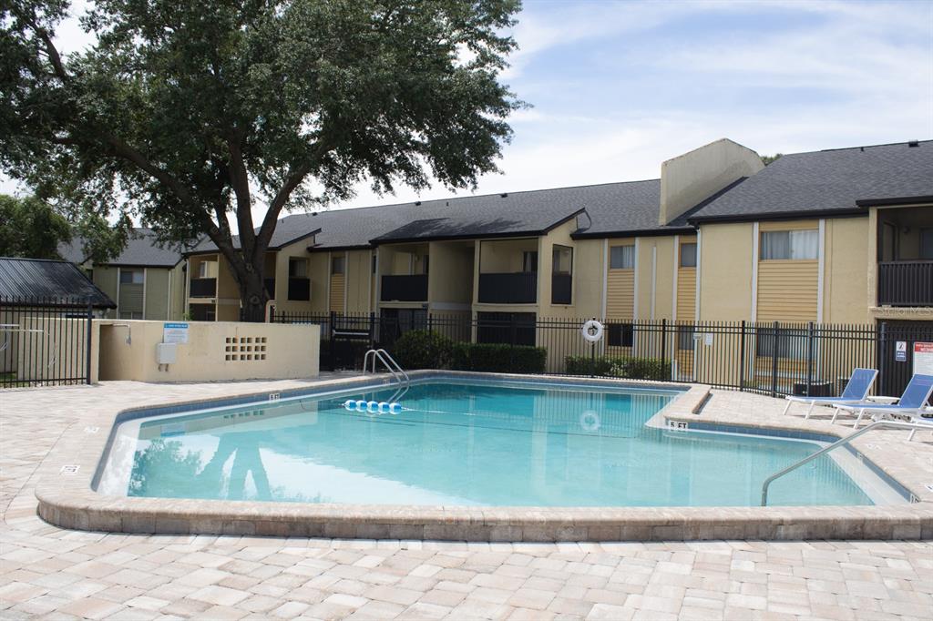 A swimming pool with a stone paver deck sits in front of a multi-story apartment building — 922 LAKE DESTINY ROAD UNIT H, ALTAMONTE SPRINGS, FL