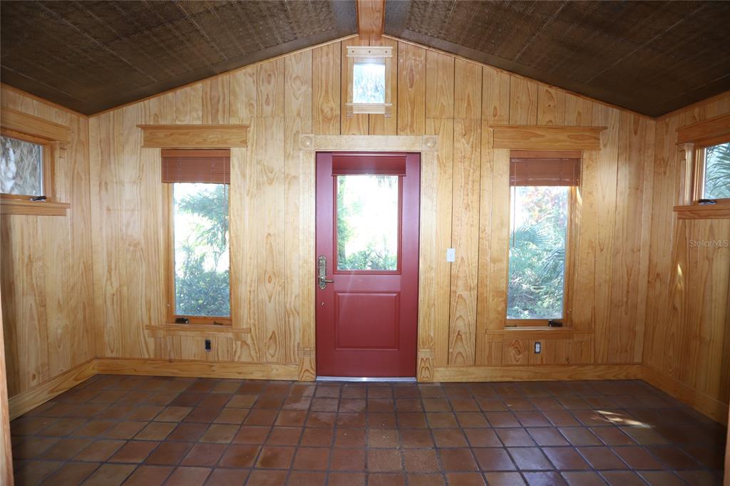 A room with wood-paneled walls, a red door, and terracotta tile flooring — 272 ORANGE STREET UNIT A-B, PALM HARBOR, FL