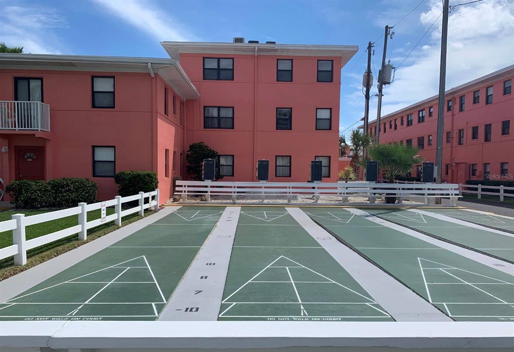 An outdoor shuffleboard court sits in front of a three-story pink apartment building — 6800 SUNSET WAY UNIT 908, ST PETE BEACH, FL