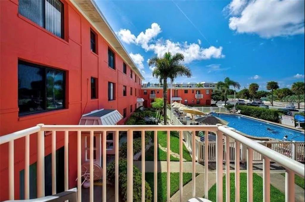 A balcony view overlooking a swimming pool and a multi-story orange apartment building — 6800 SUNSET WAY UNIT 908, ST PETE BEACH, FL