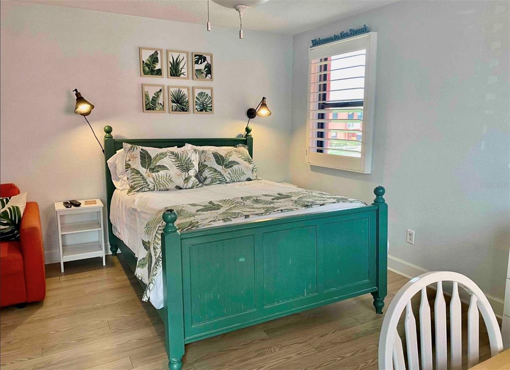 A bedroom features a green wooden bed frame, tropical bedding, wall-mounted lamps, and framed botanical art — 6800 SUNSET WAY UNIT 908, ST PETE BEACH, FL