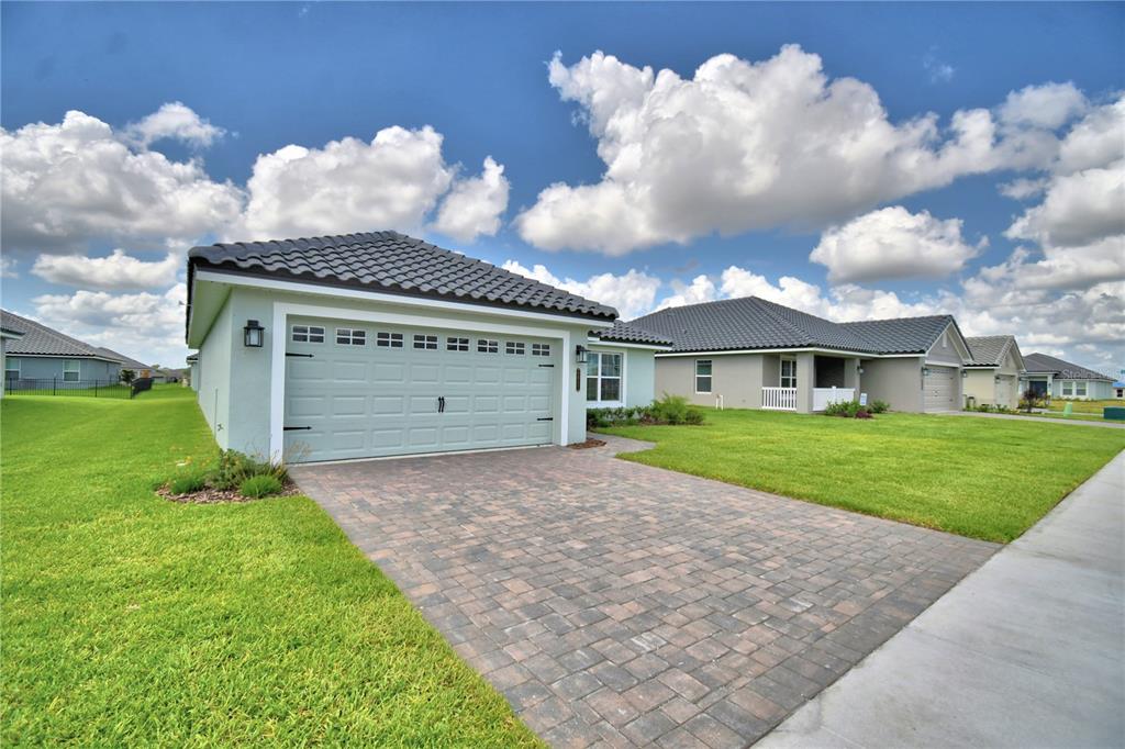 A light green house with a tiled roof and a paved driveway under a cloudy sky — 4657 GRANDVIEW GLEN DRIVE, AUBURNDALE, FL
