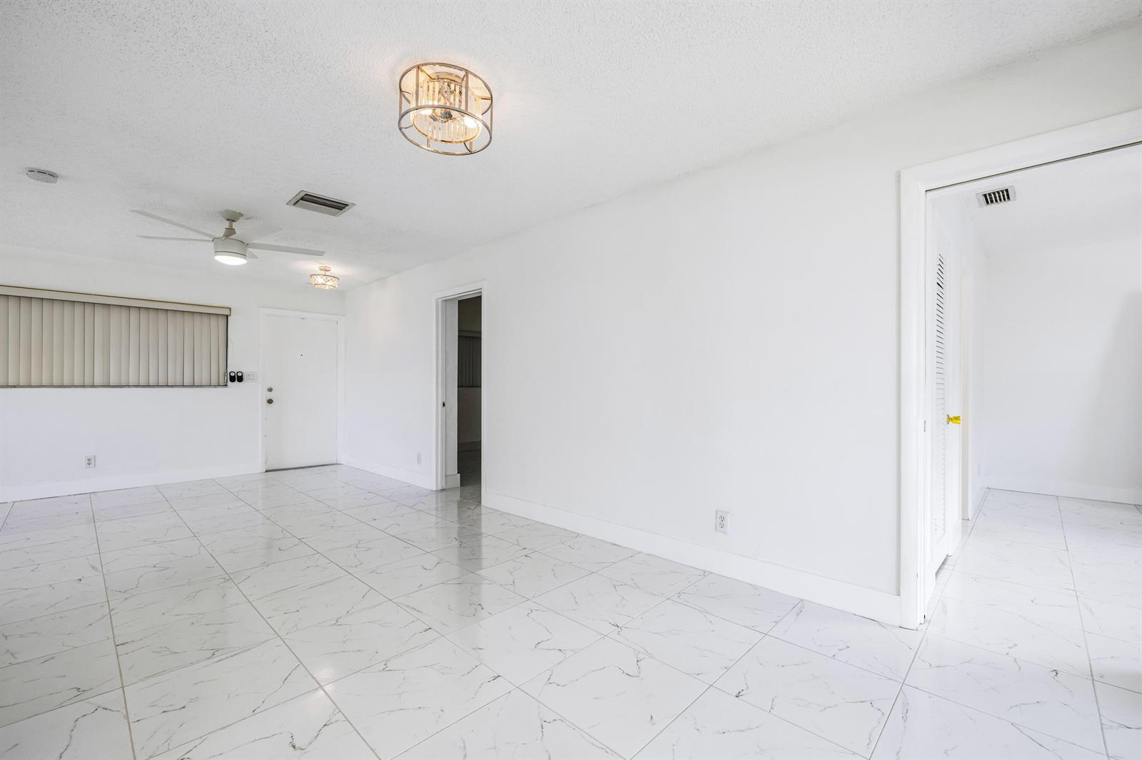 A bright, empty room features white marble-look tile flooring, white walls, and two ceiling lights — 941 Crystal Lake Drive # 207, Deerfield Beach FL 33064, DEERFIELD BEACH, FL