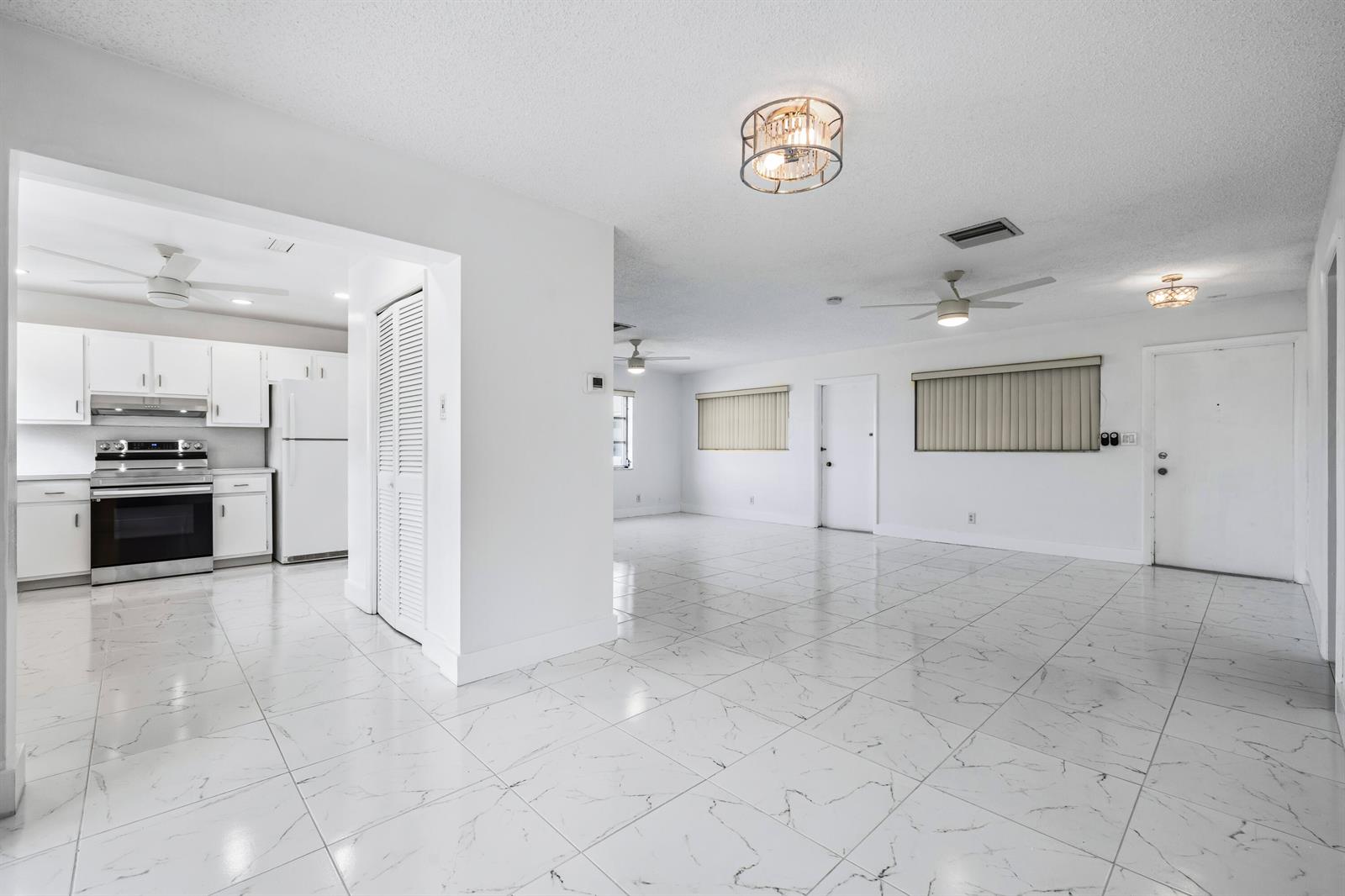 An open-concept living area with white marble-look tile floors, white walls, and a kitchen — 941 Crystal Lake Drive # 207, Deerfield Beach FL 33064, DEERFIELD BEACH, FL