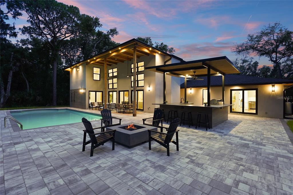 A modern two-story home features a backyard pool, fire pit, and covered outdoor kitchen area — 3325 WEBBER WOODS DRIVE, SARASOTA, FL