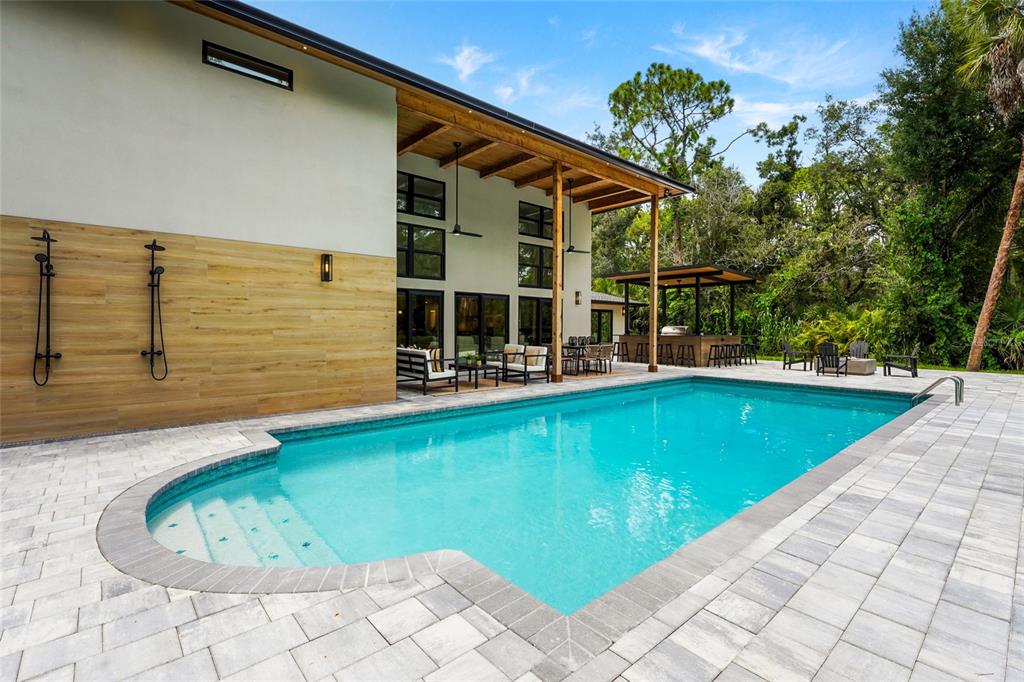 A modern house exterior features a swimming pool, outdoor showers, and a covered patio area — 3325 WEBBER WOODS DRIVE, SARASOTA, FL