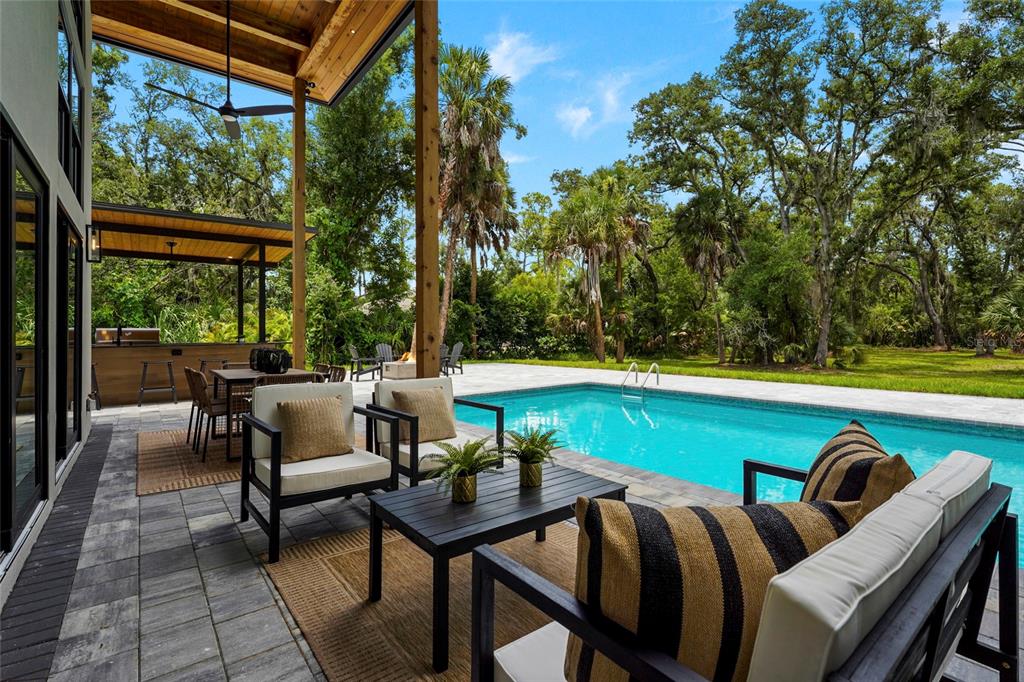 A covered patio features outdoor furniture, a dining area, and a swimming pool overlooking trees — 3325 WEBBER WOODS DRIVE, SARASOTA, FL