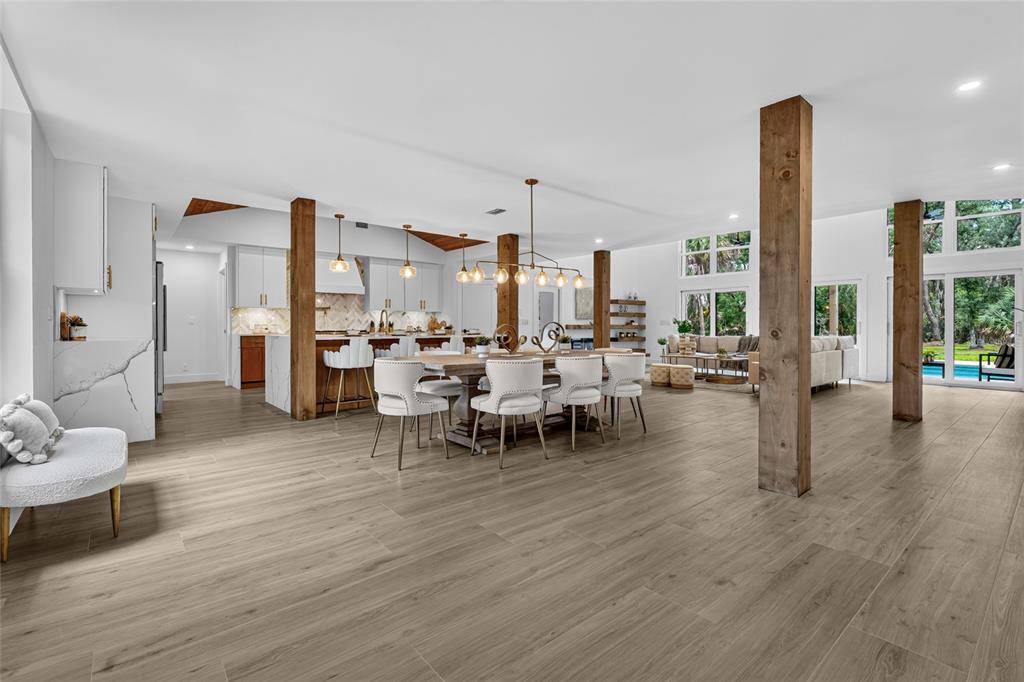 An open-concept living and dining area features wood-look tile floors, exposed wooden columns, and white cabinetry — 3325 WEBBER WOODS DRIVE, SARASOTA, FL