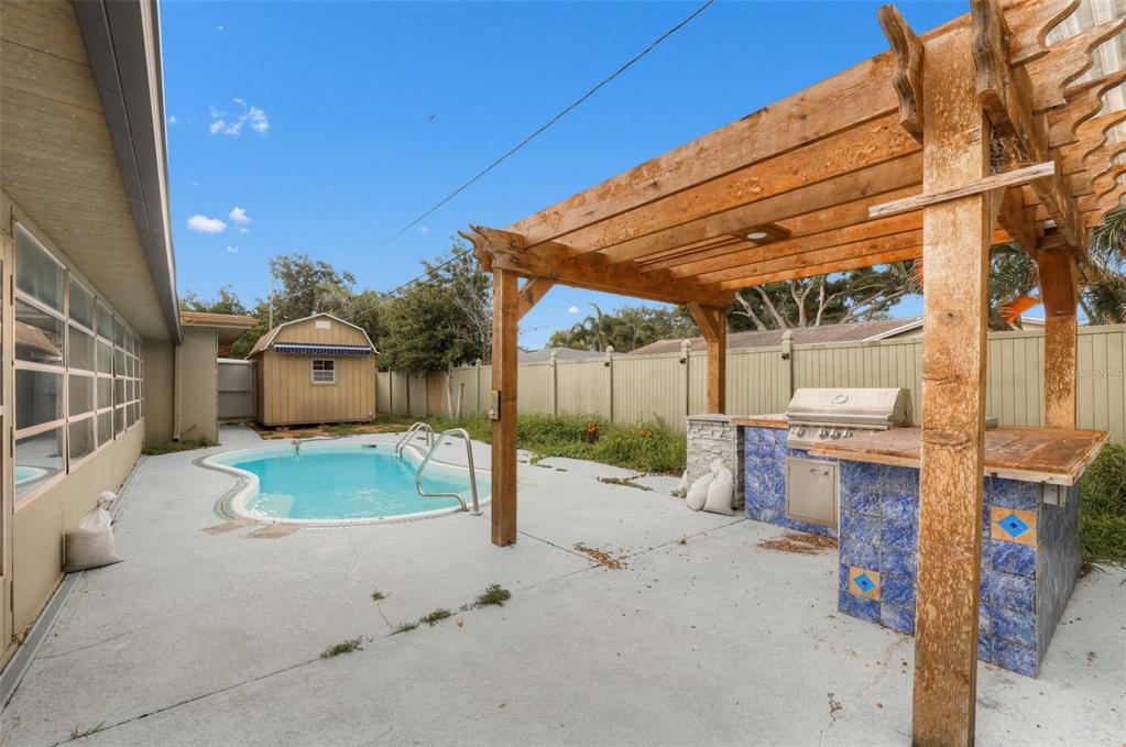A backyard features a swimming pool, a wooden pergola, and a tiled outdoor kitchen area — 6450 31ST TERRACE N, ST PETERSBURG, FL