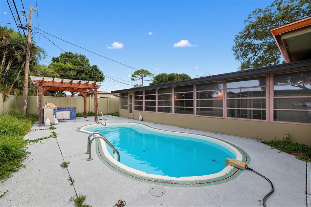A backyard features a swimming pool, a wooden pergola, and a house with screened windows — 6450 31ST TERRACE N, ST PETERSBURG, FL