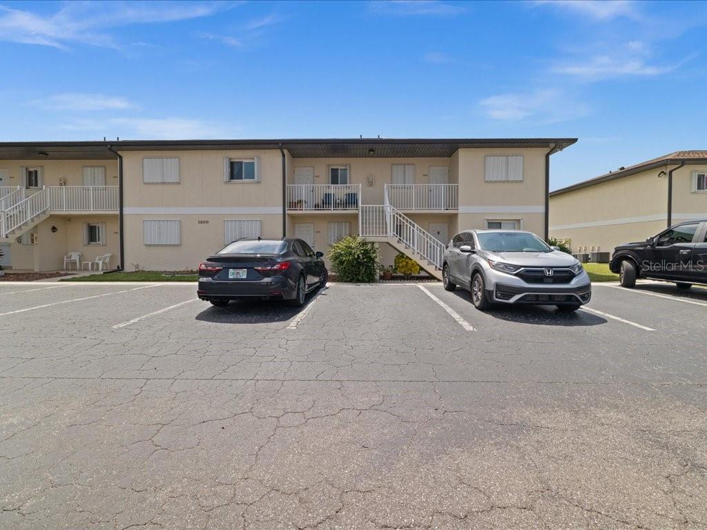 A two-story apartment building exterior with a parking lot in the foreground — 25275 RAMPART BOULEVARD UNIT 1607, PUNTA GORDA, FL