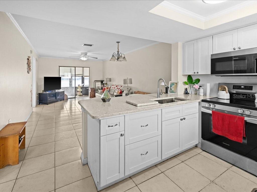 A kitchen with white cabinets and a granite-topped island overlooks an open living area — 25275 RAMPART BOULEVARD UNIT 1607, PUNTA GORDA, FL