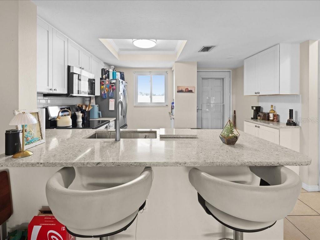 A kitchen with white cabinets, a granite island, and two bar stools — 25275 RAMPART BOULEVARD UNIT 1607, PUNTA GORDA, FL