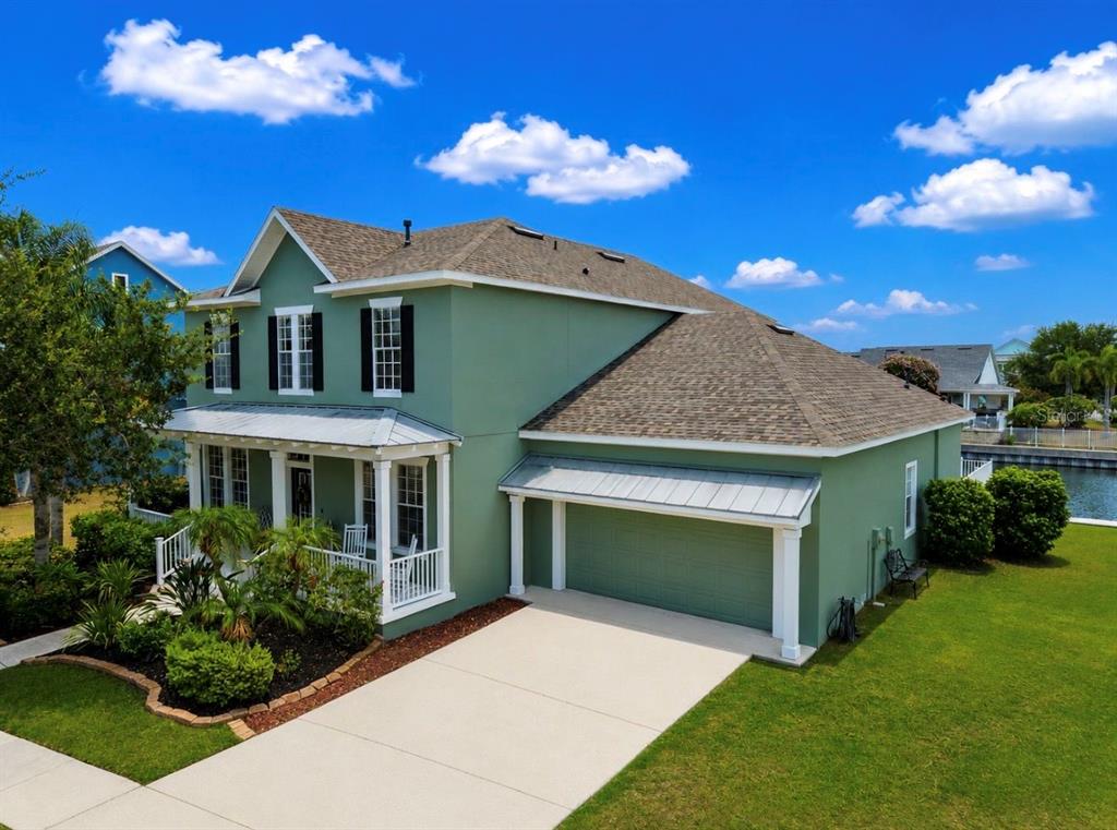 A two-story green house with a front porch, attached garage, and a shingled roof — 5709 SEA TROUT PLACE, APOLLO BEACH, FL