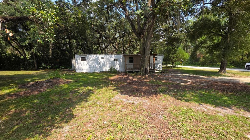A single-story mobile home sits on a grassy lot surrounded by large, mature trees — 49 NE 472ND AVENUE, OLD TOWN, FL