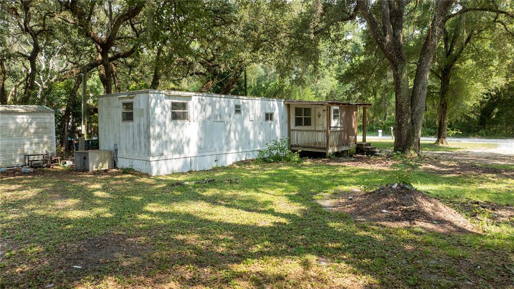 A weathered mobile home sits on a grassy lot shaded by large, mature trees — 49 NE 472ND AVENUE, OLD TOWN, FL