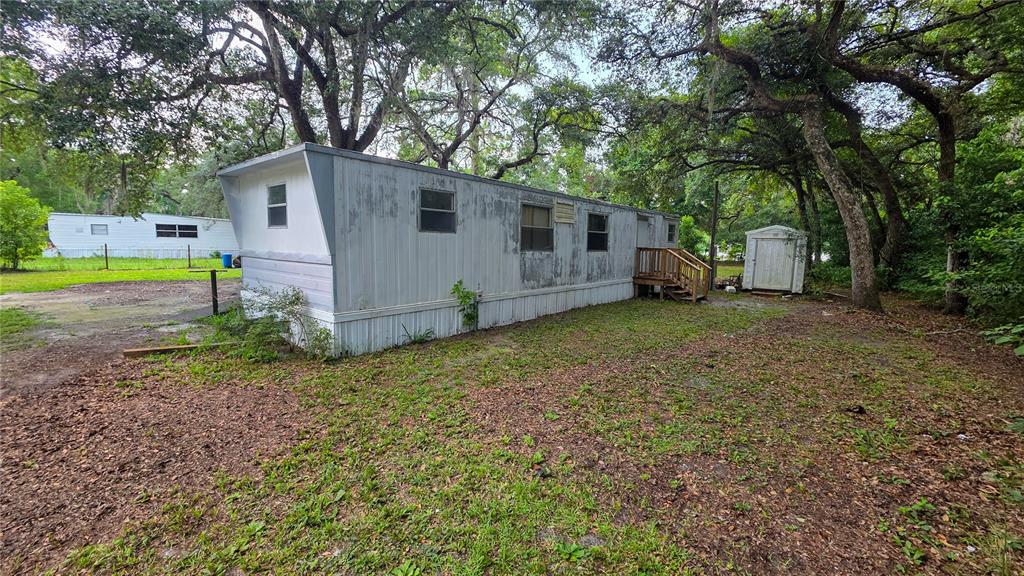 A weathered mobile home sits on a grassy lot with a small shed and trees — 49 NE 472ND AVENUE, OLD TOWN, FL