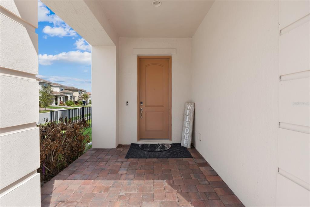 A covered front porch with brick pavers leads to a tan front door — 8148 CLEOBURY DRIVE, ORLANDO, FL