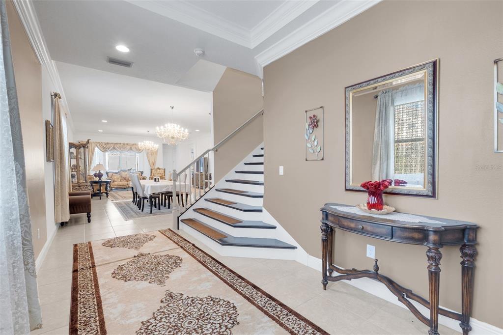 A foyer features a staircase with wood treads, a console table, and a dining area beyond — 8148 CLEOBURY DRIVE, ORLANDO, FL