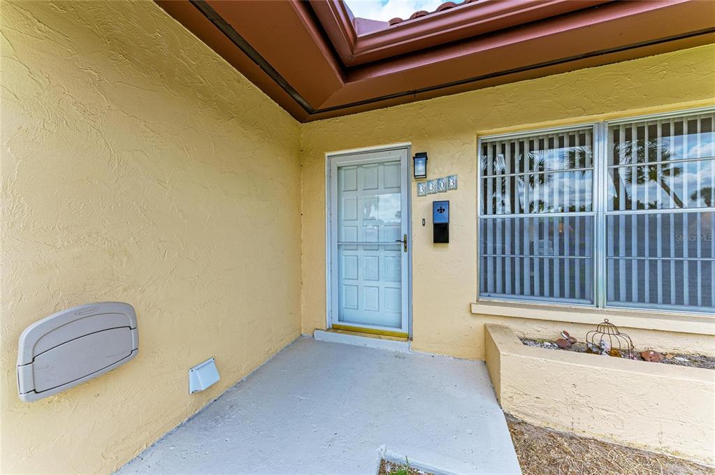 A yellow stucco exterior features a front door with a storm door and a window — 3303 CHICAGO AVENUE, BRADENTON, FL