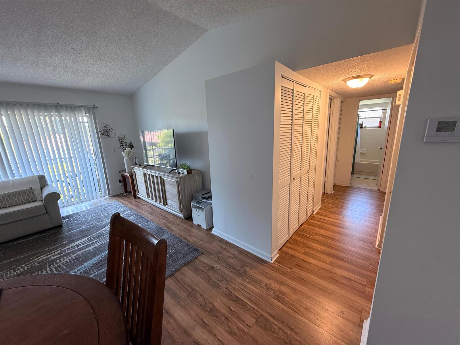 A living room with wood-look flooring, a white closet, and a view into a bathroom — 9923 Three Lakes Circle # h, Boca Raton FL 33428, BOCA RATON, FL