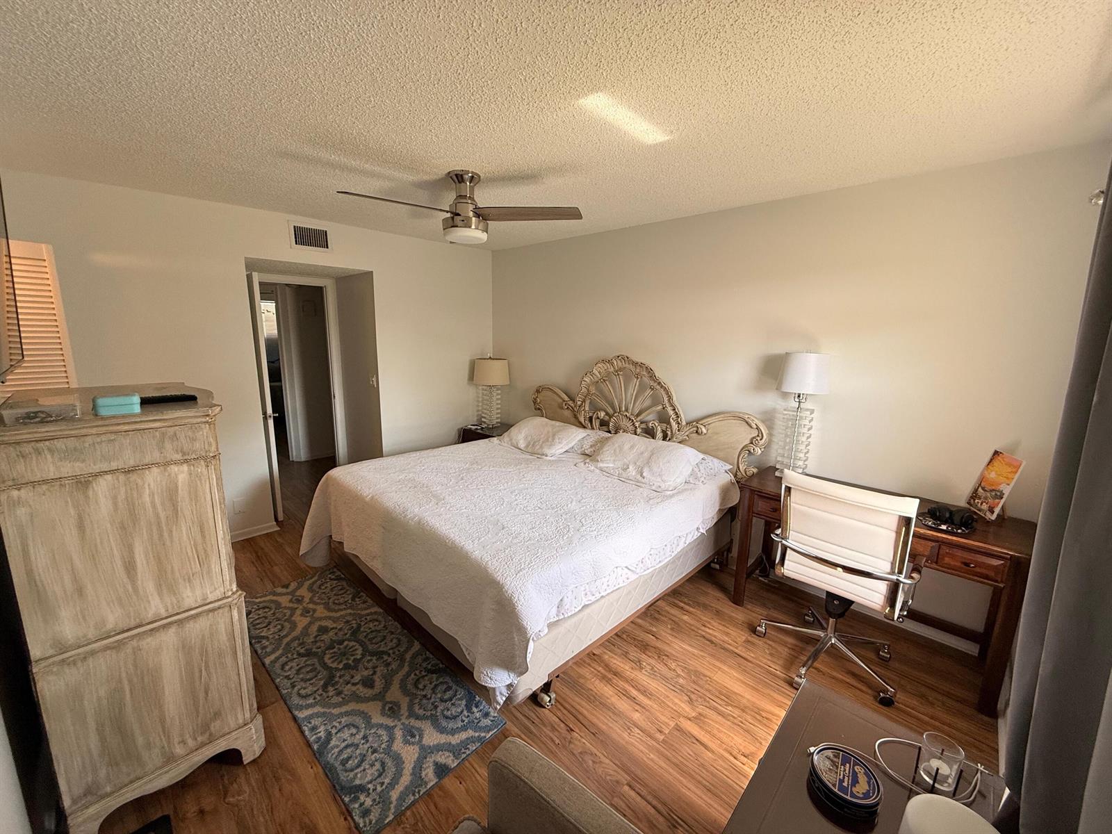A bedroom with wood-look flooring, a ceiling fan, a white bed, and a desk — 9923 Three Lakes Circle # h, Boca Raton FL 33428, BOCA RATON, FL