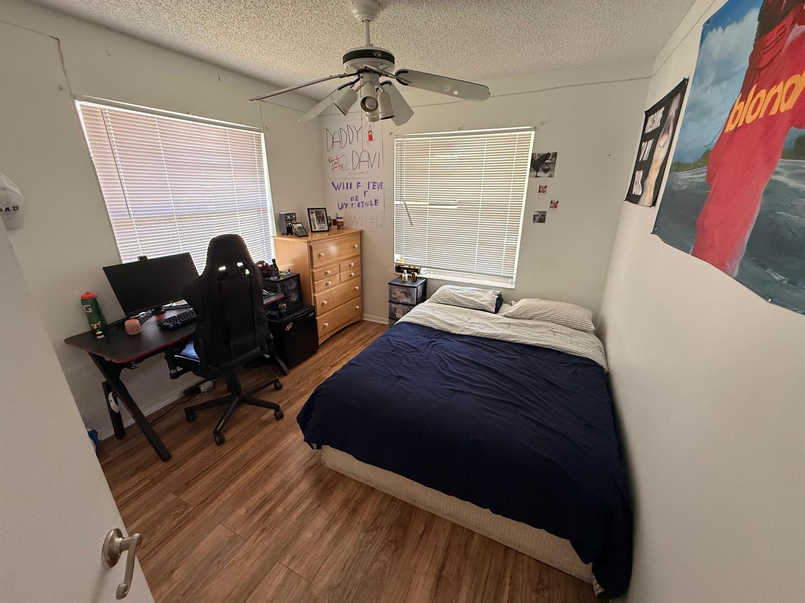 A bedroom with wood-look flooring, a bed, a desk with a gaming chair, and two windows — 9923 Three Lakes Circle # h, Boca Raton FL 33428, BOCA RATON, FL