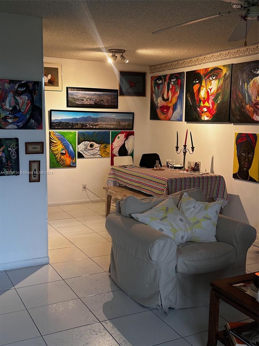 A living and dining area features tiled floors, a beige armchair, and numerous colorful wall paintings — 3771 Environ Blvd # 151, Lauderhill FL 33319, LAUDERHILL, FL
